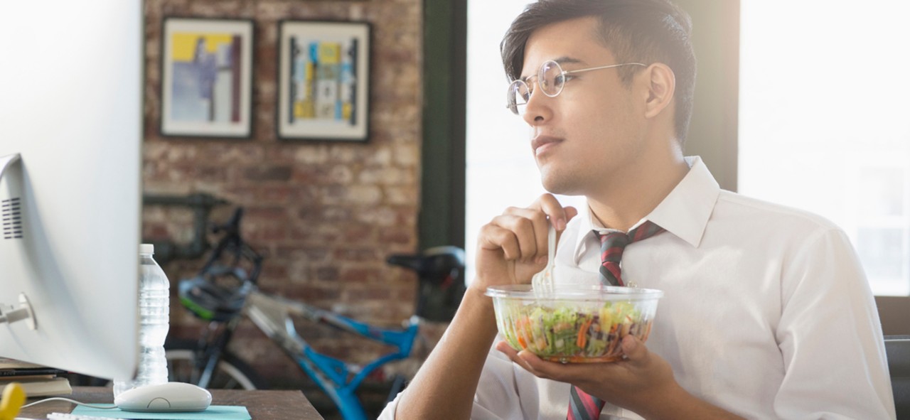 Mixed Race businessman using computer and eating salad at desk